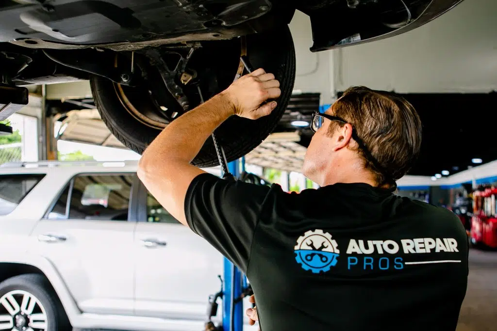 Technician inspecting underside of vehicle with flashlight in repair shop.